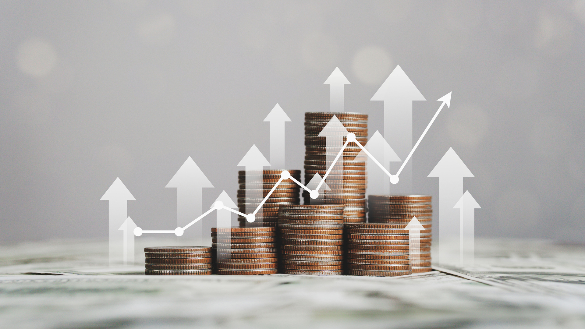 coins stacked up with an overlay of white upward facing arrows and a line graph trending upwards