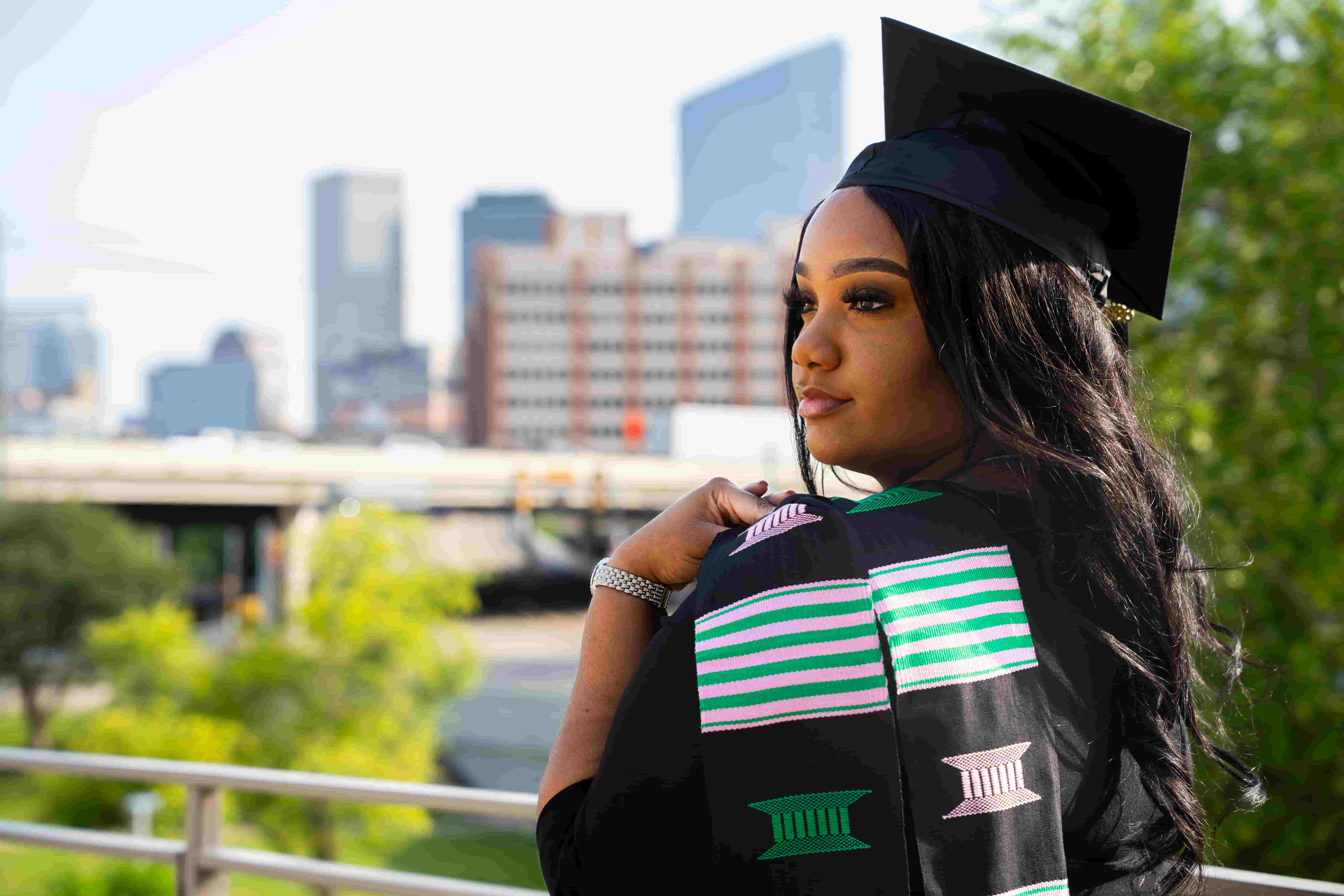 female uhd graduate in cap and gown with a cityscape background