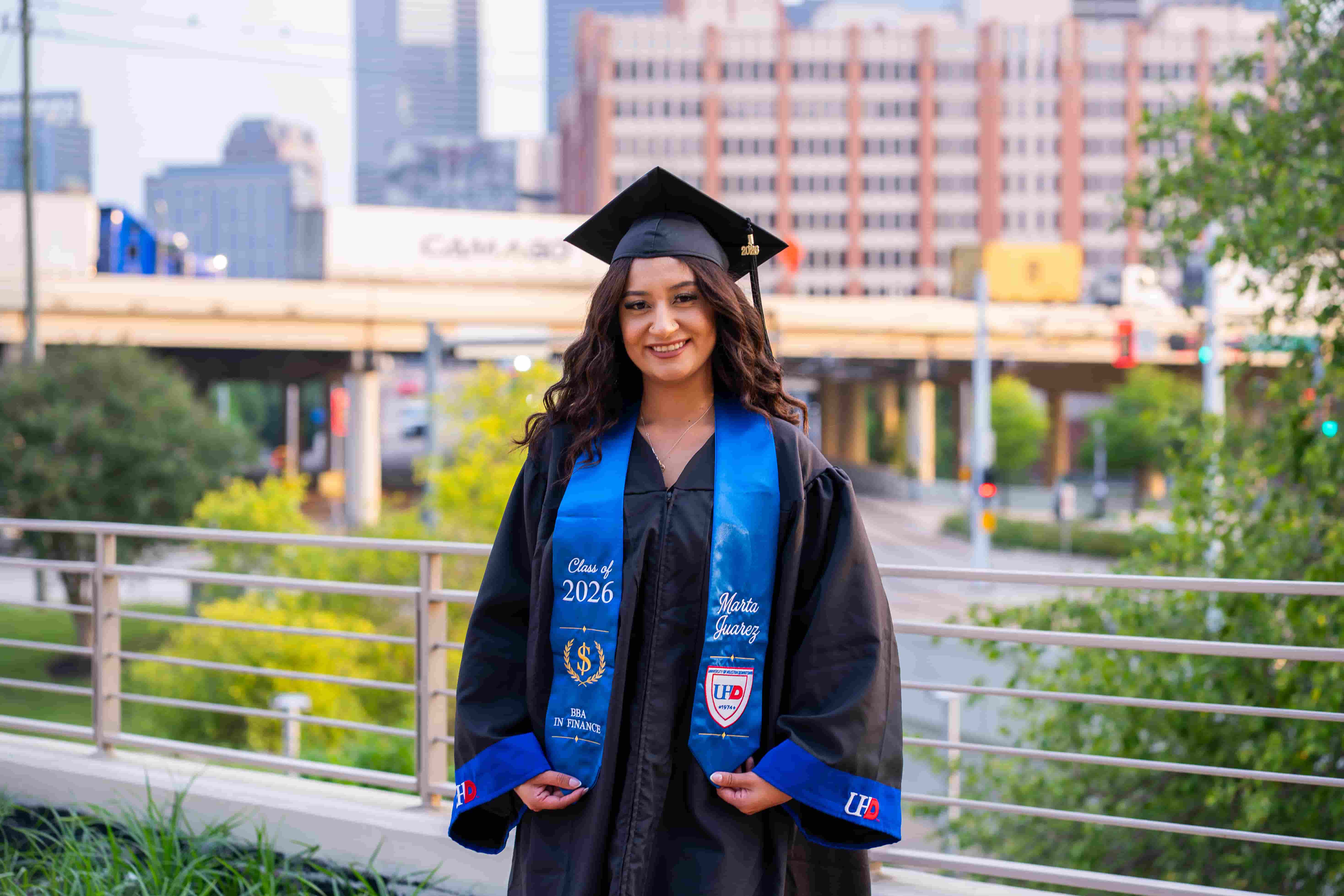 female graduate in her cap and gown with a city scape background