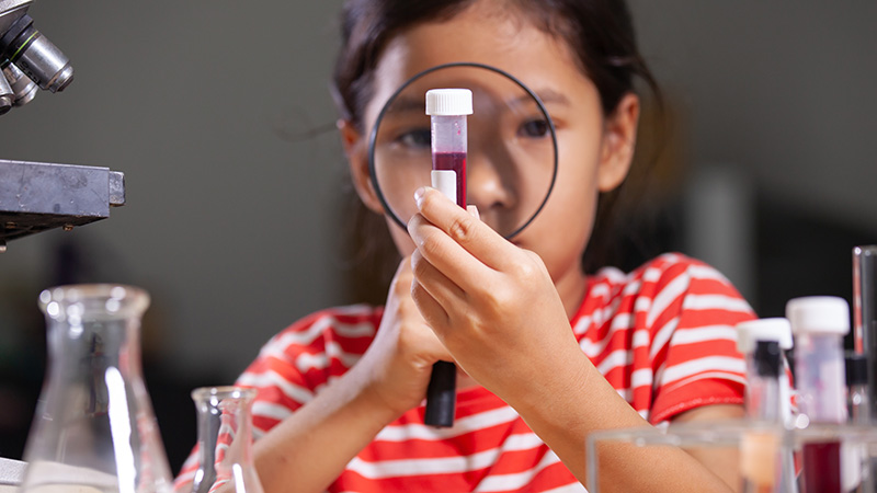Girl holding a magnifying glass up to vial of fluid