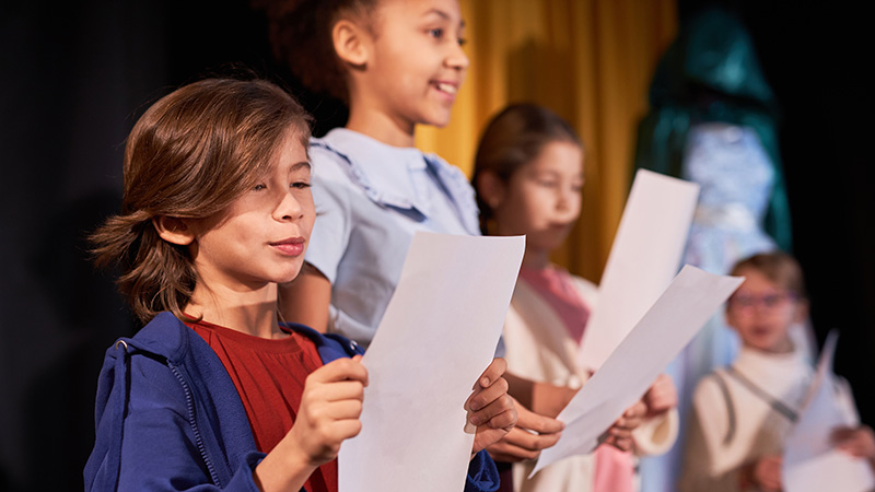 Kids holding scripts and performing on stage