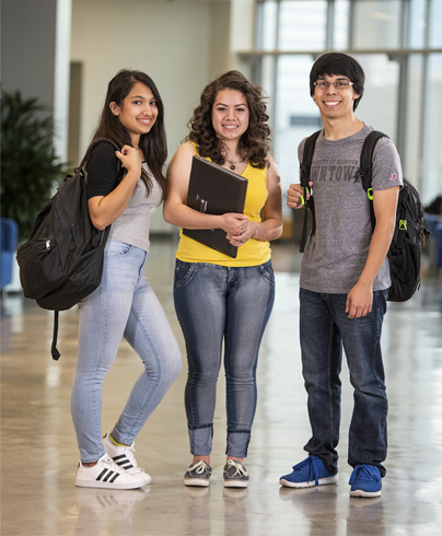 Three UHD students standing in the Wlecome Center with back backs and books