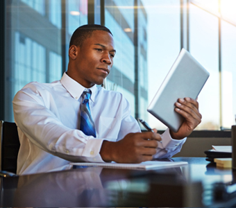 professional African American male in an office writing on a notepad and holding a tablet