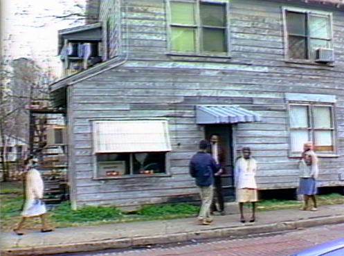Still from Alligator Horses film, people in front of an older wooden building. 