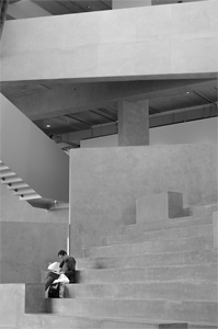 black and white photo of person sitting on steps with concrete architecture