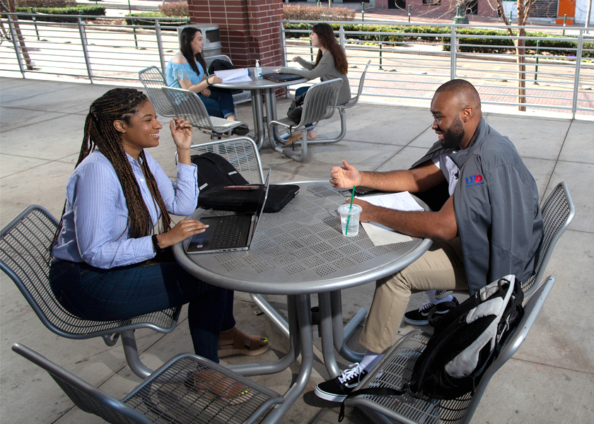 UHD students at tables talking and doing homework outside
