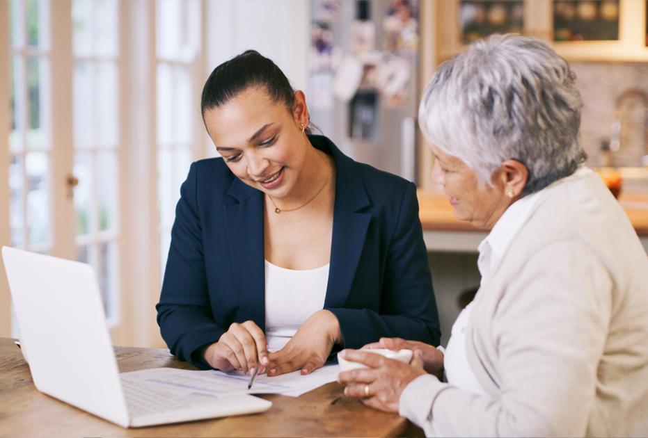 woman  at laptop computer shows an older woman something on a peice of paper