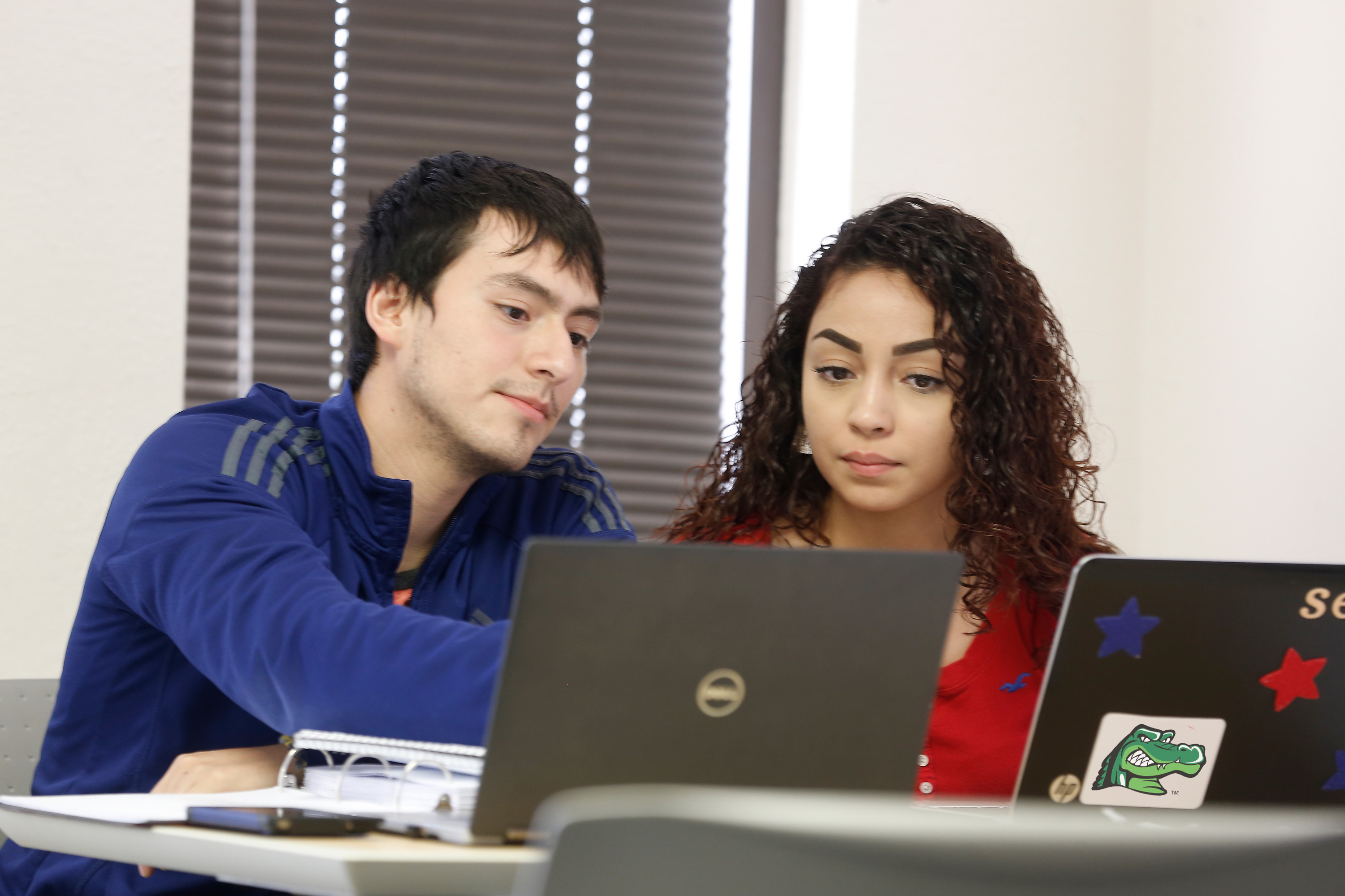 two UHD students on laptops talking with each other