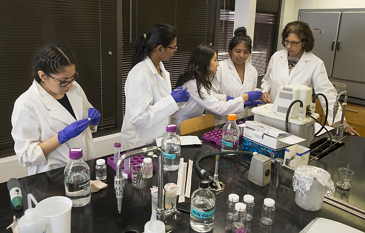 Doctor and students in a lab using suringes and tubes to test water samples.