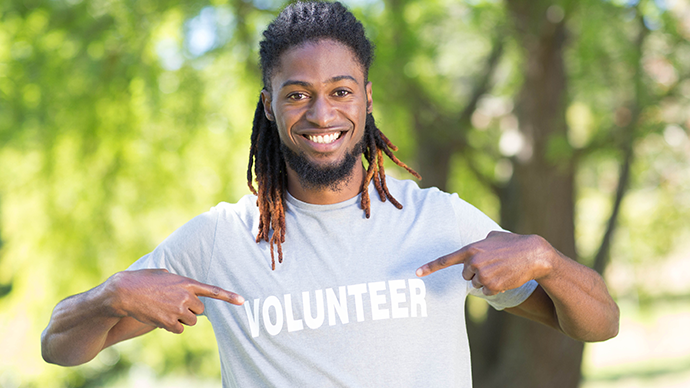 Volunteer at a park smiling pointing at their volunteer t-shirt
