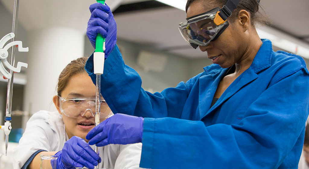 Two lab techs adding a liquid to test beaker.