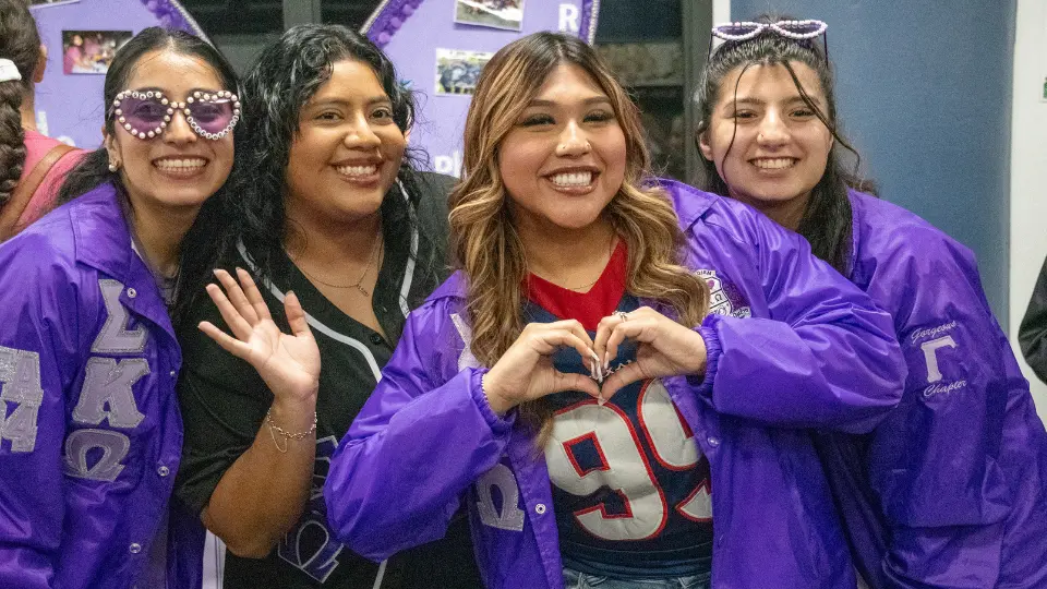 A group of women wearing purple jackets and sunglasses, smiling together outdoors.