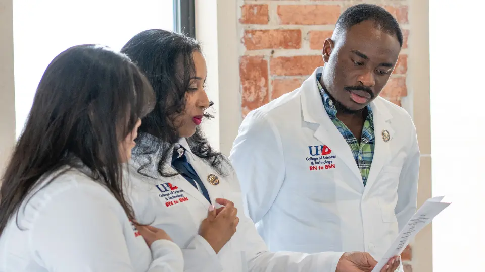 Three adults in UHD lab coats reviewing paperwork