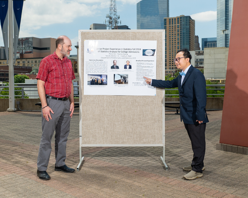 Timothy Redl stands aside a senior research post for the impact learning and community engagement showcase. Thomas Duong points to their poster. 