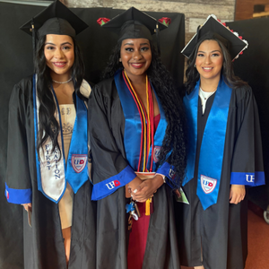 Three University of Houston-Downtown students smile while wearing stoles, caps, cords, and gowns 