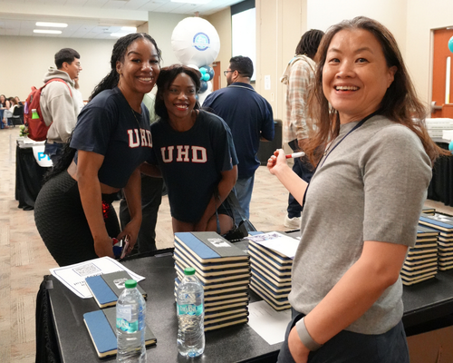 Two students and members of the cheerleading squad smile at a microcredential table with a faculty member at the university of houston downtown in houston, texas