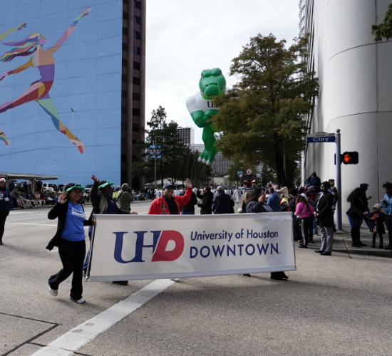 Members of the University of Houston Downtown community hold a banner that reads "University of Houston-Downtown" during the HEB Thanksgiving Day Parade