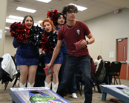 A university student throws a bean bag at a bean bag toss game while members of the gatorettes watch at the university of houston-downtown in downtown houston