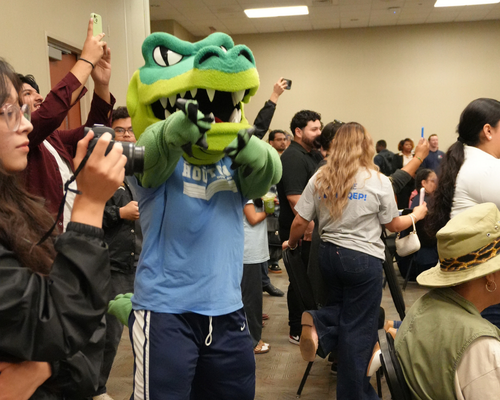 university of houston downtown mascot ed-u-gator the alligator points while the crowd takes photographs of the university of houston-downtown cheerleaders while they perform a routine at the quality enhancement plan pep rally