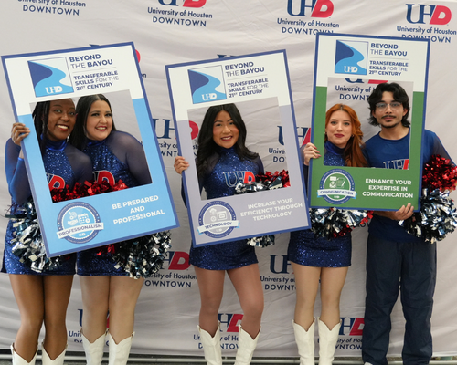 Students and members of university of houston-downtown's dance team, the gatorettes, hold photo frames for the quality enhancement plan in front of a step and repeat with the university's logo 