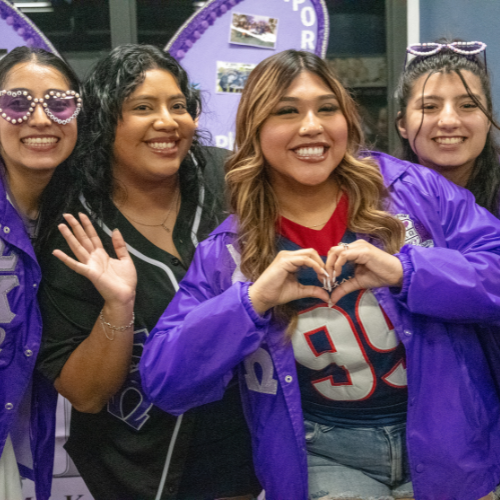 Four university of houston-downtown students in a sorority smile while tabling  
