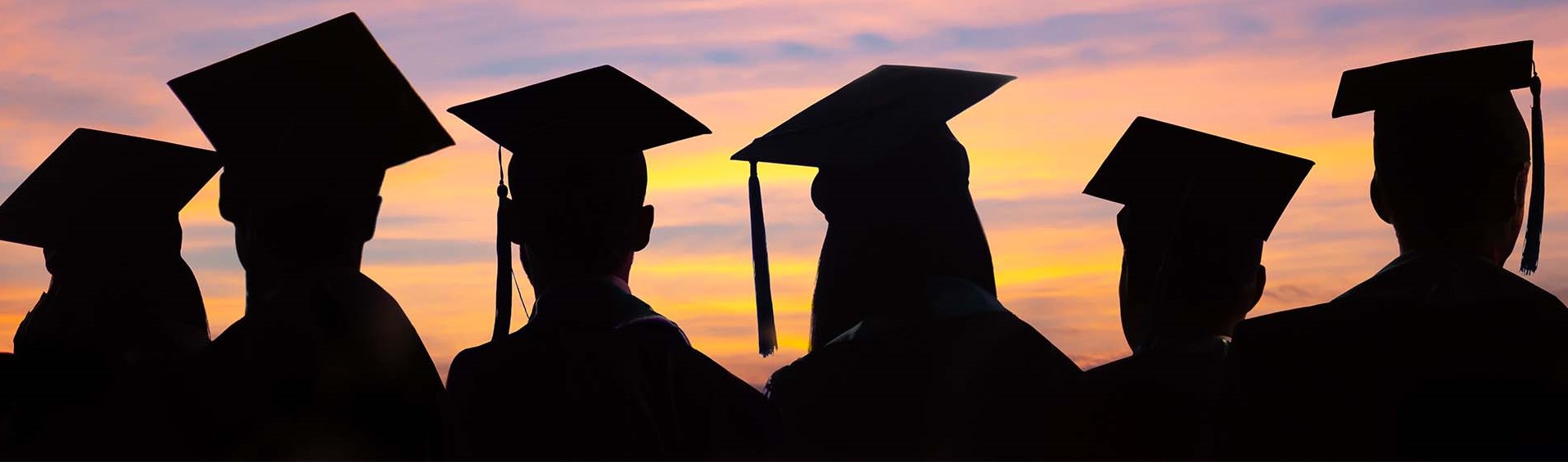 Silhouettes of students in their caps and gowns against a sunrise