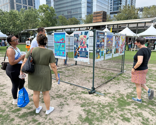 Adults view posters by graphic design students from the University of Houston-Downtown at Earth Day 2026 at Discovery Green 