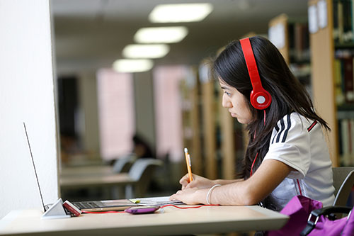 A student studying in the library with headphones on.