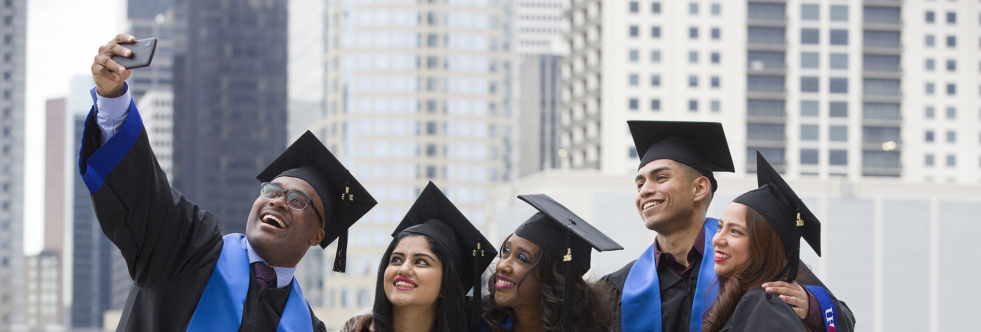 Goal 1 Banner: Students posing for a group selfie wearing graduation gowns.