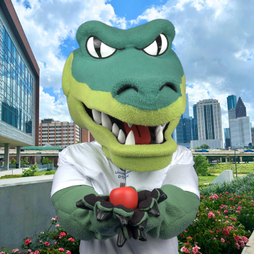 university of houston downtown mascot ed u gator holds an apple in front of the college of sciences and technology at the university of houston downtown