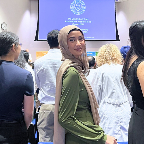 Hafsa Khalil smiles alongside fellow medical school students. Projecter behind Khalil reads,