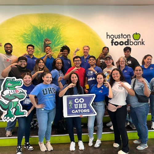 University of Houston Downtown students, staff and faculty smile while holding UHD branded signs at the Houston Food Bank for Marilyn Davies College of Business