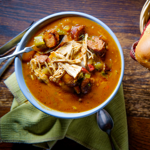 A bowl of chicken and sausage soup, napkin, and spoon