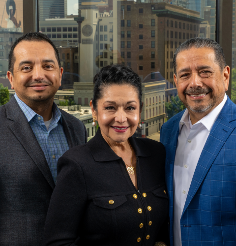 University of Houston-Downtown alums Robert Mendoza Jr, Paula Mendoza, and Robert Mendoza smile with the Downtown Houston skyline behind them in Houston, Texas.