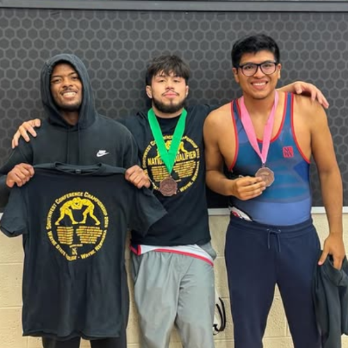 Three members of the University of Houston-Downtown's wrestling teams. Two members have medals around their necks. 