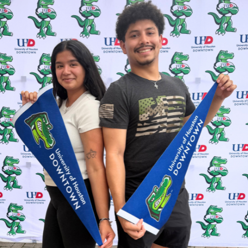 Two high school seniors hold up university of houston-downtown pennants at the university's commitment day in april 2026