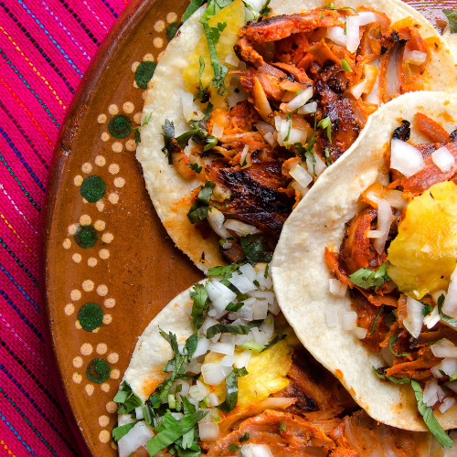 Three street tacos filled with meat, cilantro, pineapple, and onion on a hand painted plate 